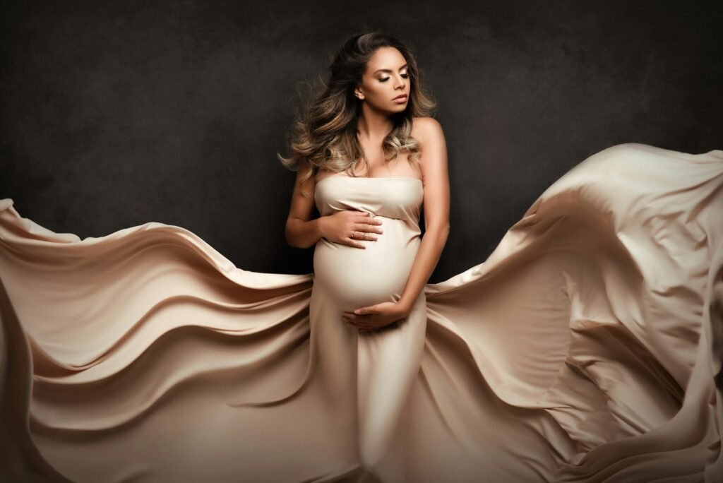 Captivating maternity portrait of a woman in a flowing dress with a regal pose on a dark background.